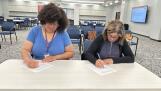 Northwest Suburban High School District 214 Education Association President Nichole Anderson, left, and school board President Alva Kreutzer ink a new five-year teachers’ contract Friday morning.